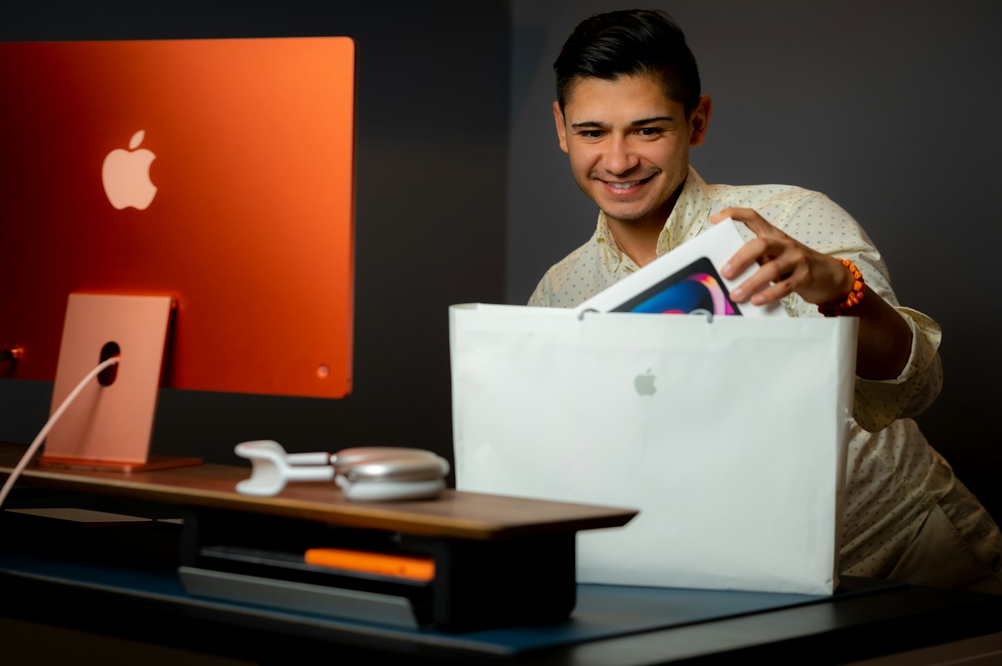 Hombre saca feliz un nuevo gadget de una bolsa de compras en un escritorio.