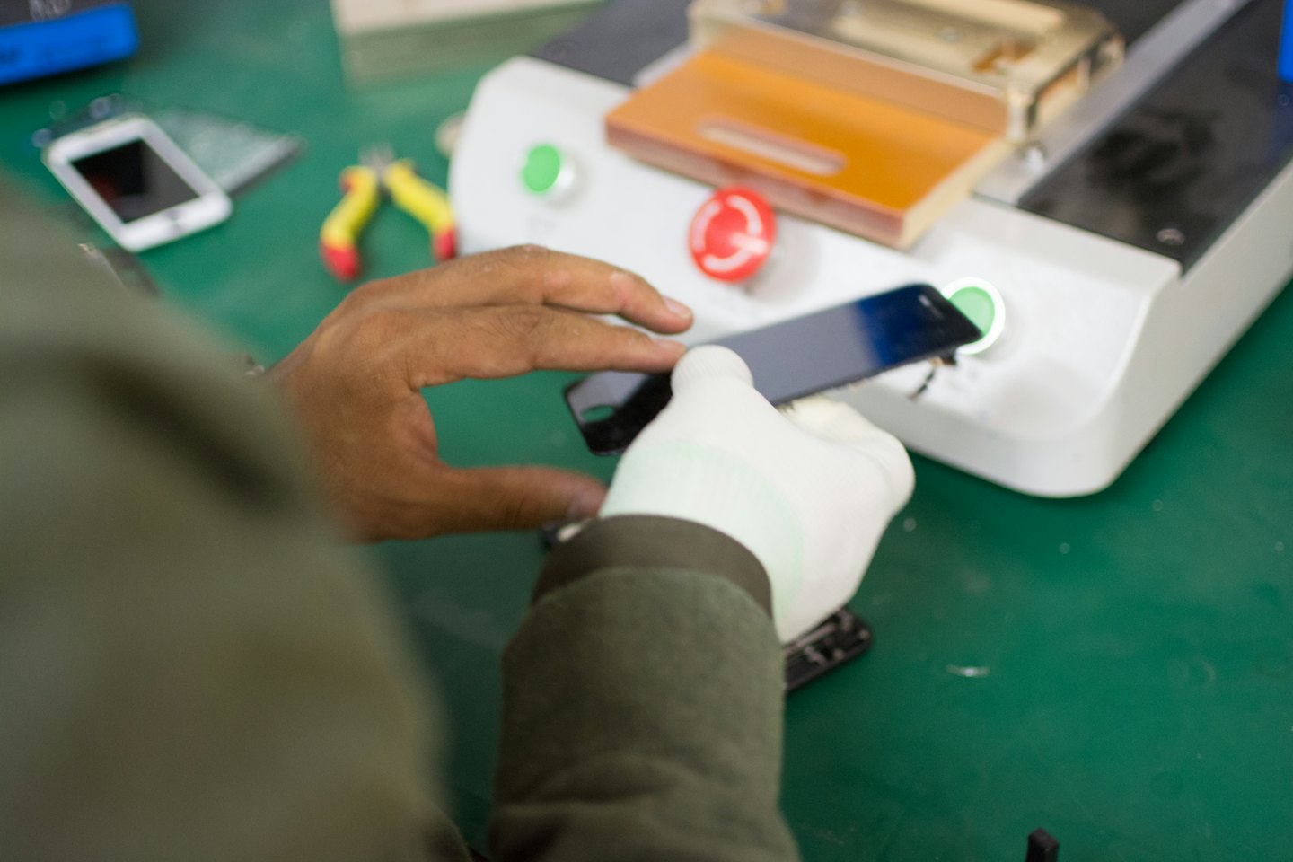 Técnico reparando un smartphone en un banco de trabajo verde.